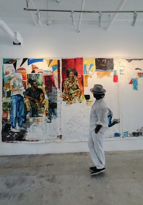 Yared Nigussu in a white shirt and fedora, standing before a large work in progress in the studio